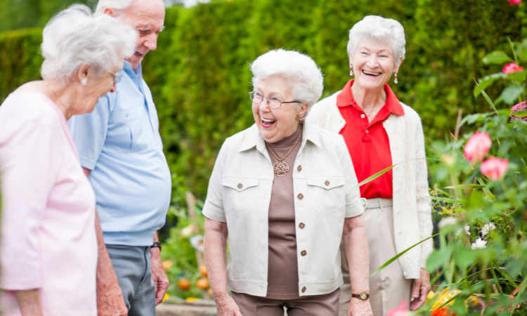 Fyra glada seniorer ute i en trädgård